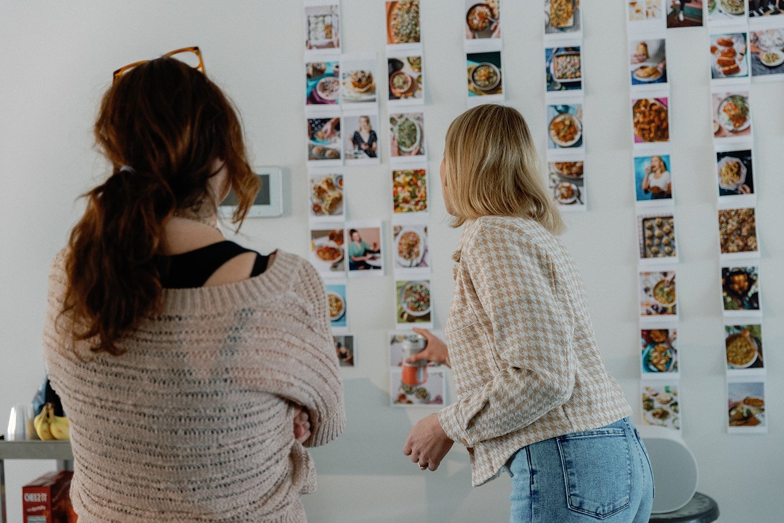 Monique Volz of Ambitious Kitchen and a designer looking at a wall of cookbook photos