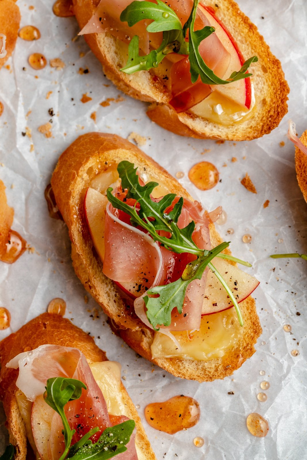 apple and brie crostini with hot honey on parchment paper