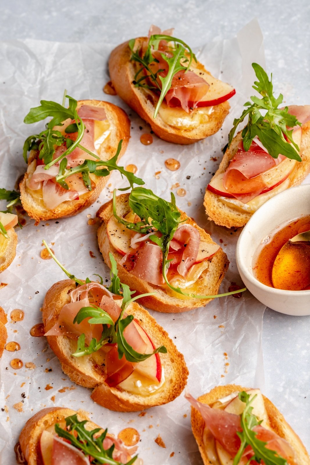 apple and brie crostini with prosciutto and arugula on parchment paper