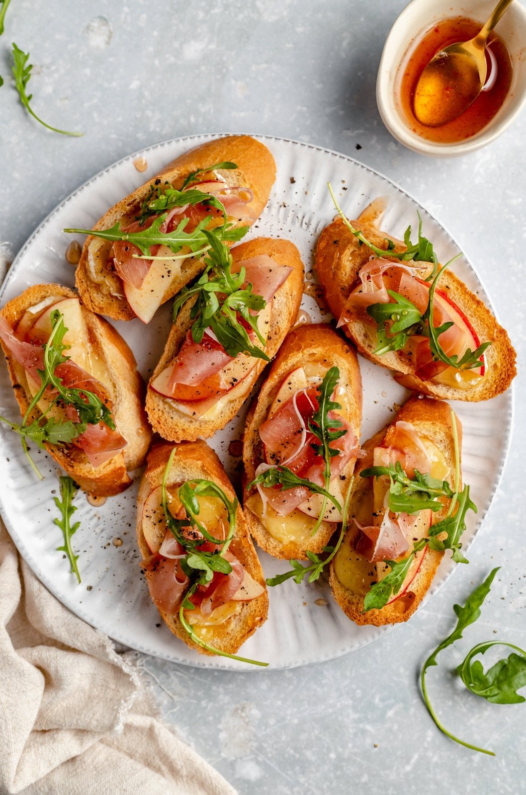 easy apple and brie crostini with prosciutto and arugula on a plate