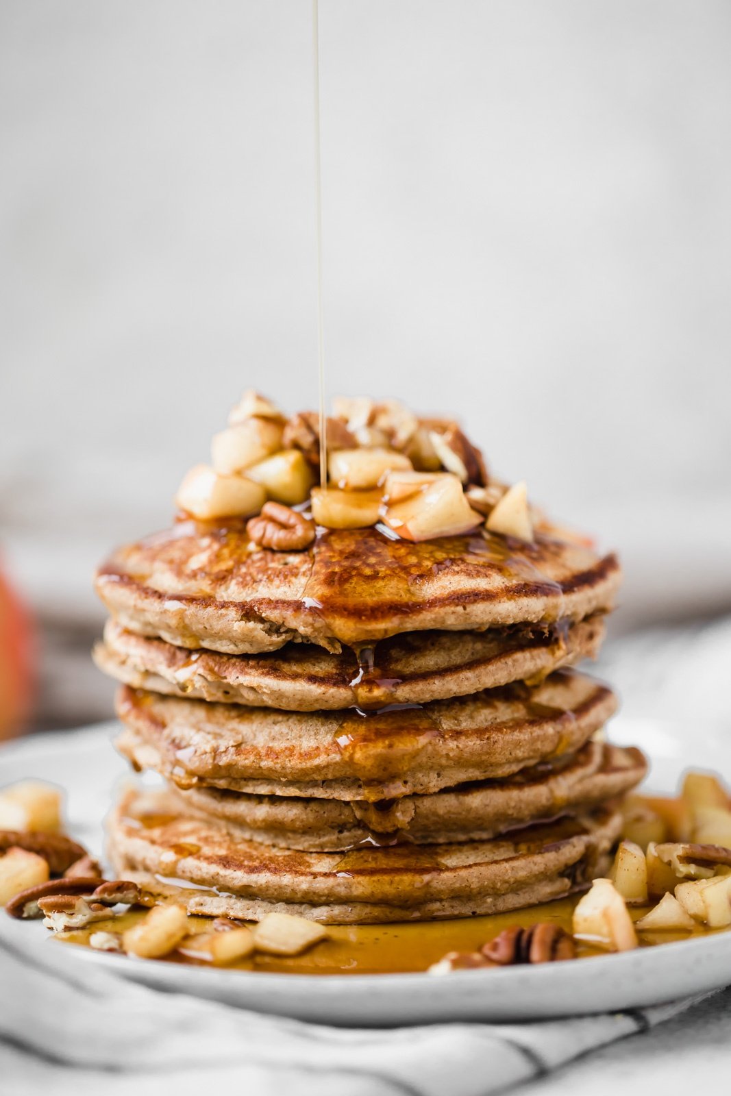 healthy apple pancakes on a plate with maple syrup being poured on top