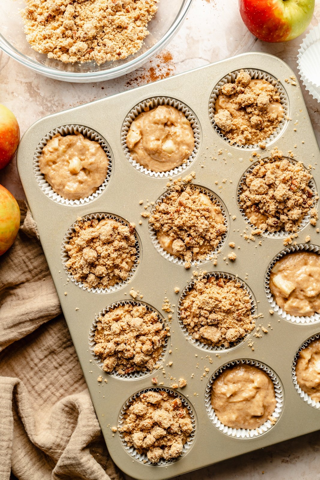 unbaked apple muffins with a crumble topping in a muffin tin