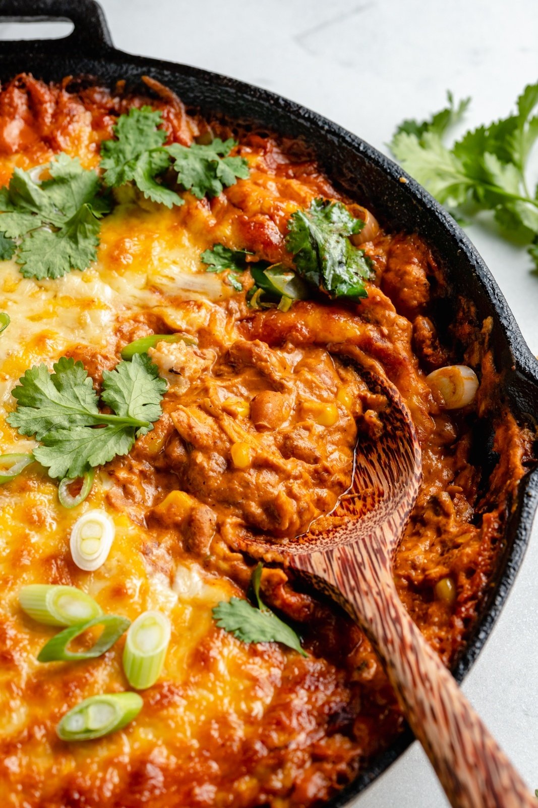 cheesy enchilada bean dip in a skillet with a wooden spoon