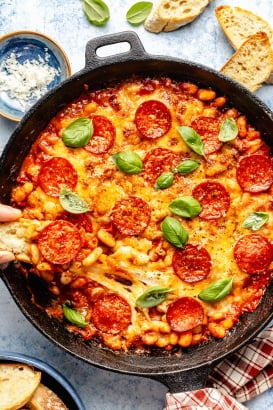 dipping crostini in a skillet with a pepperoni white bean bake