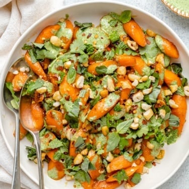 caramelized garlic carrots in a bowl with fresh herbs and green sauce