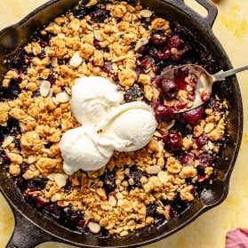 cherry crisp topped with ice cream in a skillet with a spoon