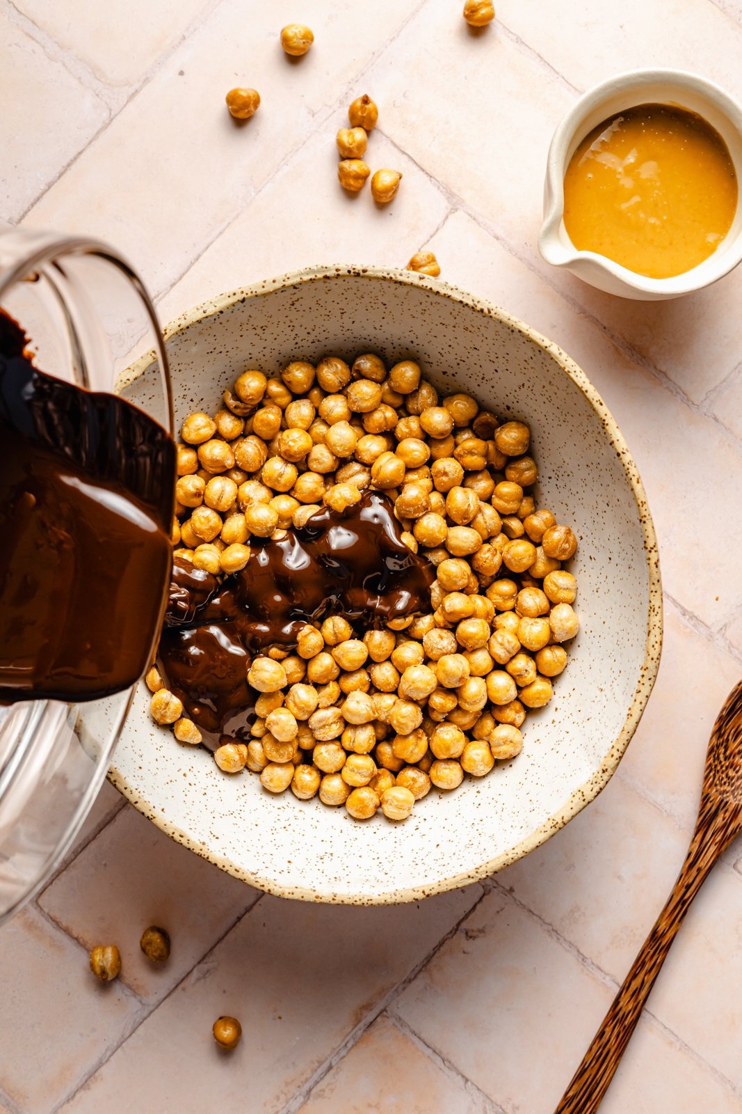 pouring melted chocolate into a bowl of roasted chickpeas