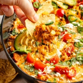 scooping southwest bean dip out of a skillet with a tortilla chip