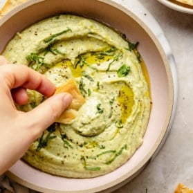 dipping a pita chip into a bowl of white bean hummus