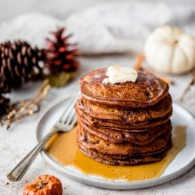 stack of gingerbread pancakes on a plate next to mini pumpkins