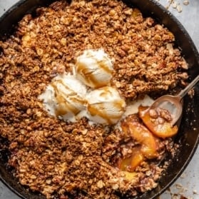 gluten free peach crisp in a skillet topped with ice cream