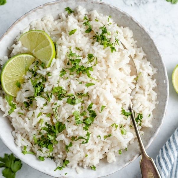 coconut rice in a bowl with cilantro and lime wedges