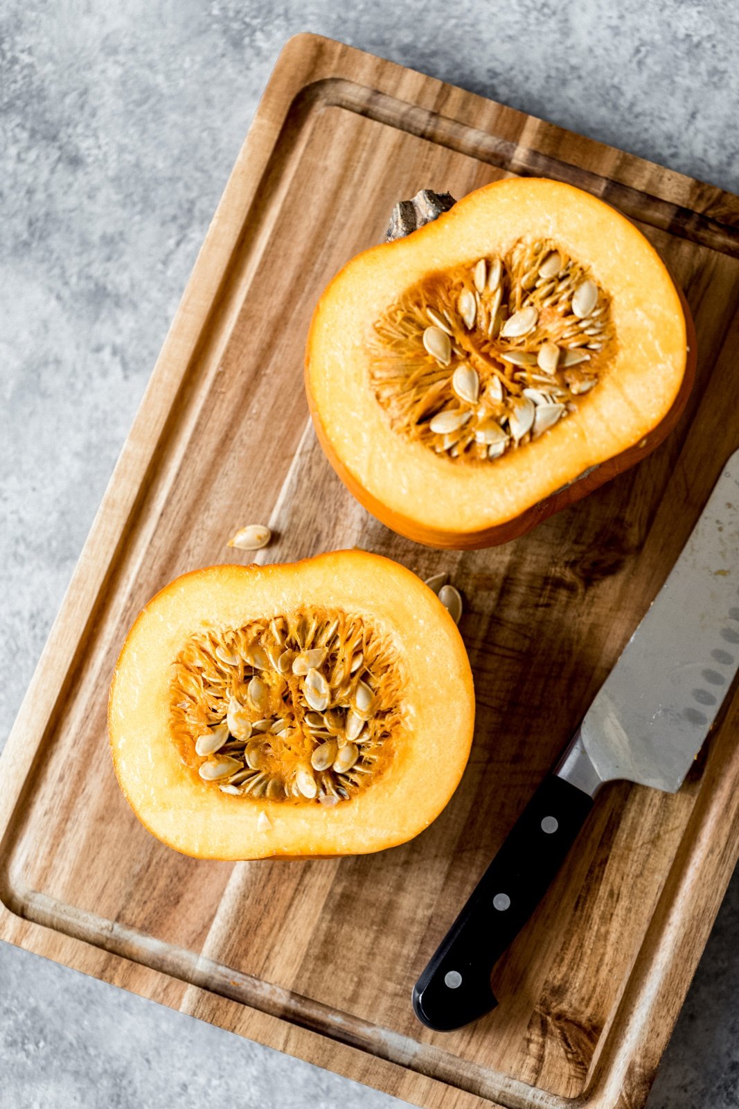 pumpkin cut in half on a cutting board with a knife