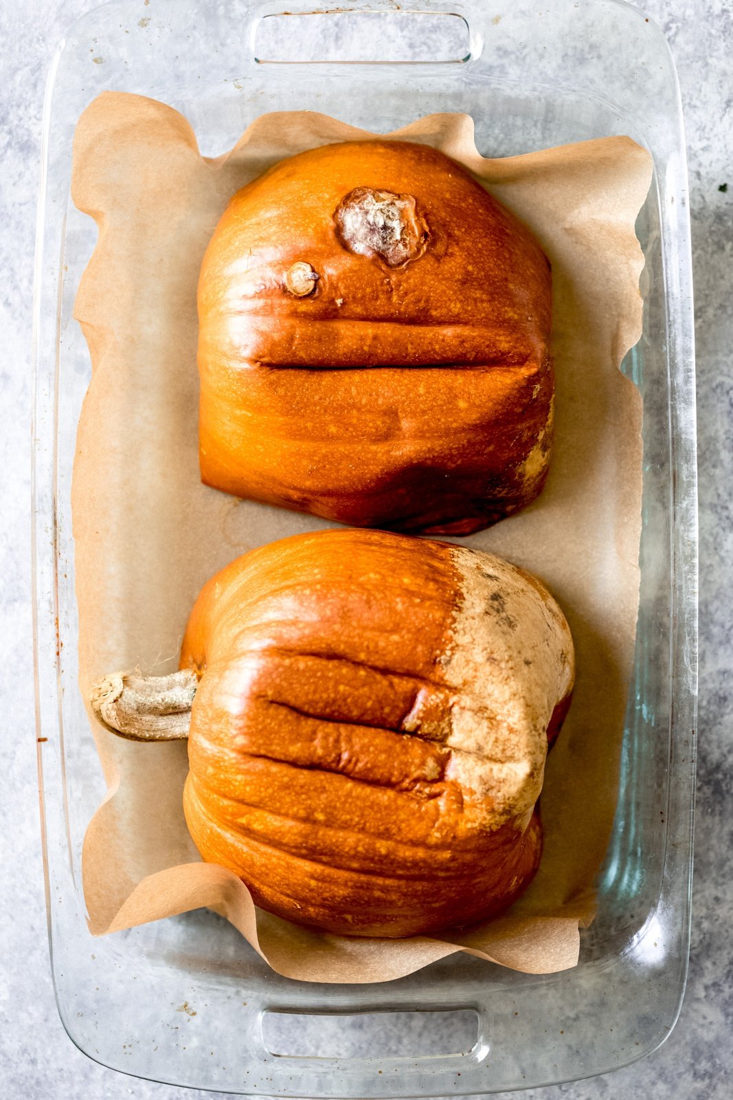 two pumpkin halves face down in a glass baking pan