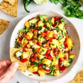 overhead shot of a chip dipping into a bowl of mango salsa