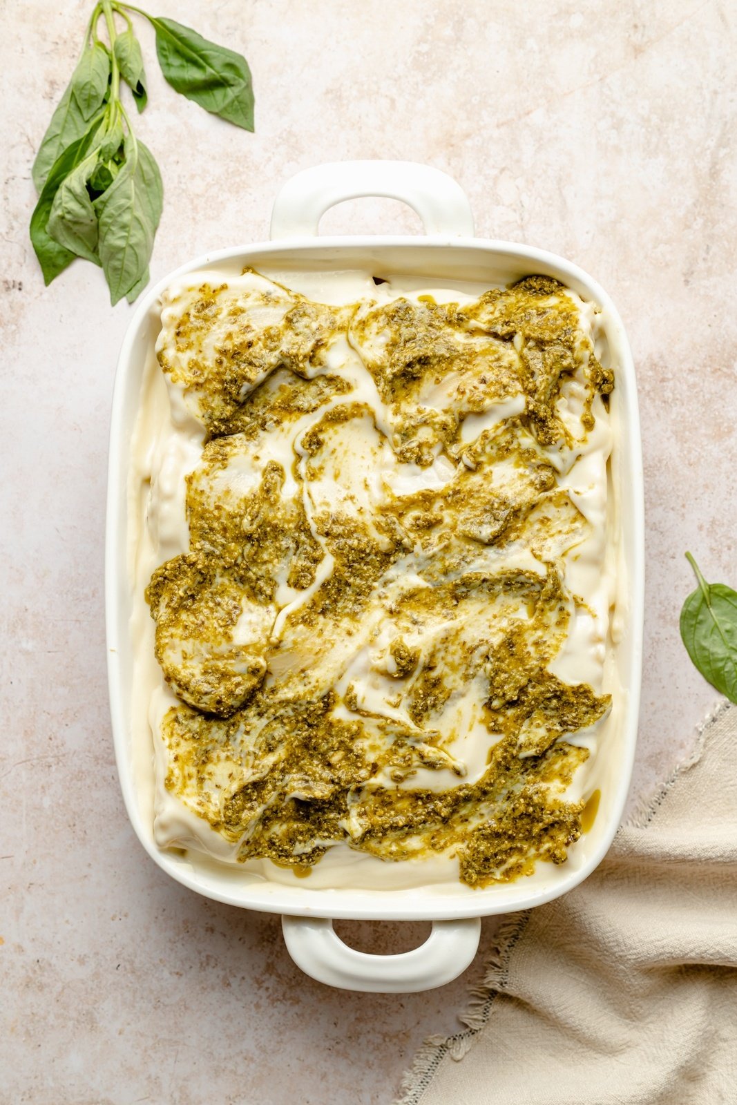 unbaked chicken lasagna in a pan topped with pesto