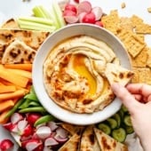 dipping pita into a bowl of roasted garlic hummus surrounded by veggies