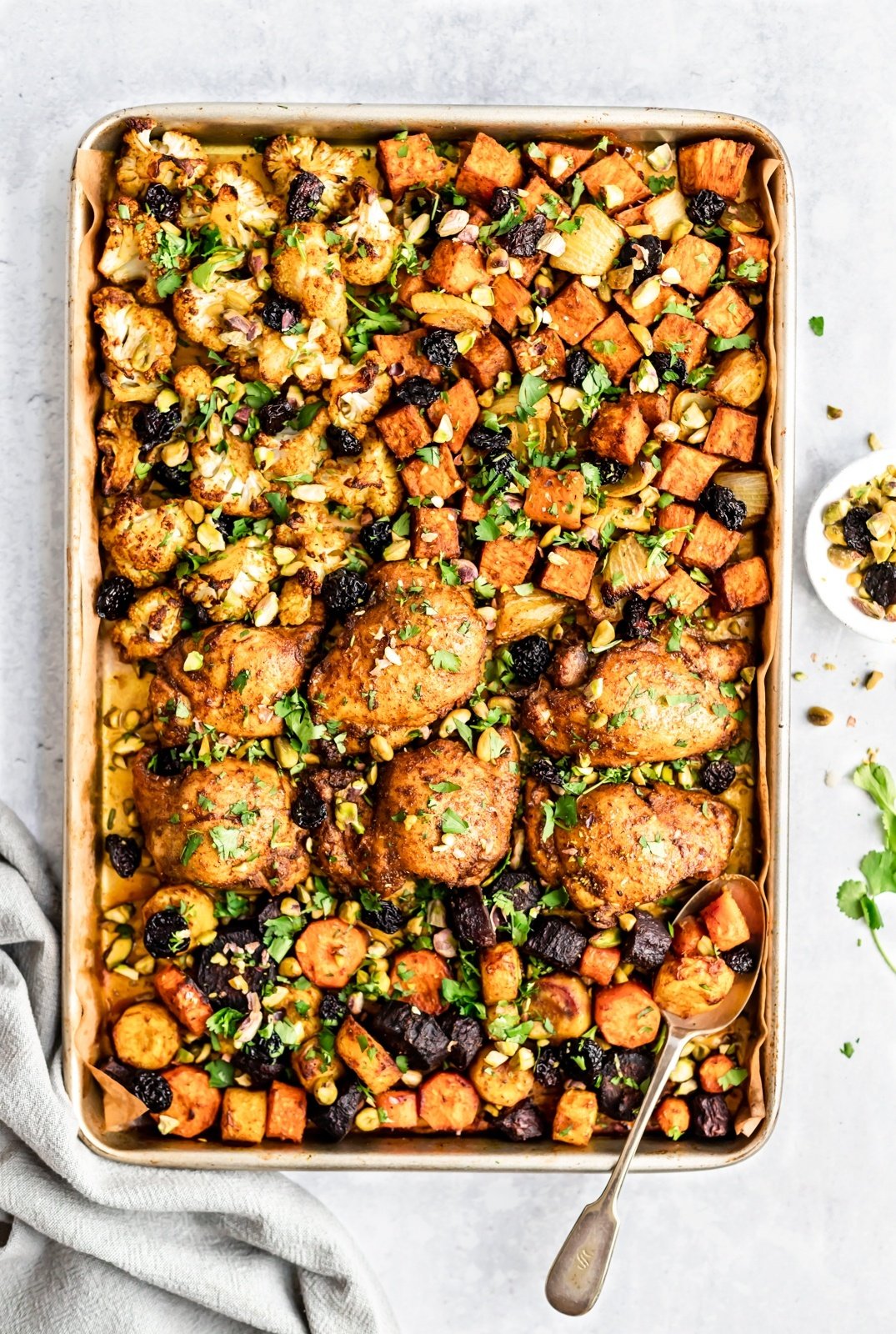 moroccan sheet pan chicken and veggies on a pan with a spoon