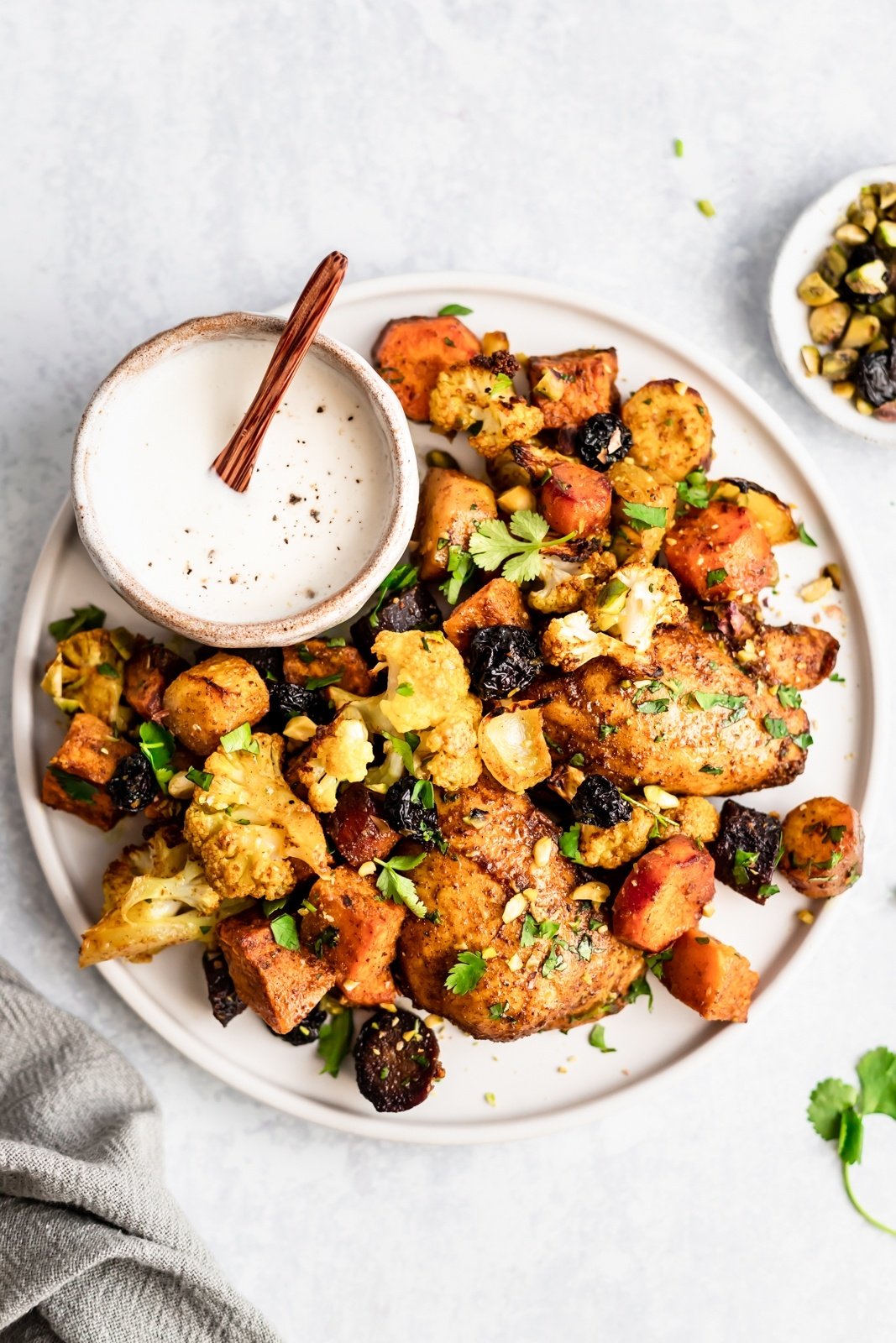 sheet pan moroccan chicken and veggies on a plate next to yogurt sauce