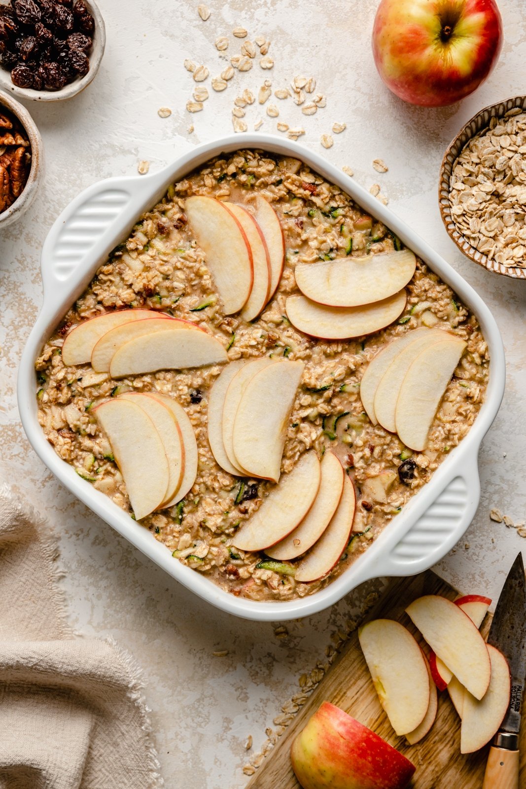 unbaked apple zucchini baked oatmeal in a pan topped with sliced apples