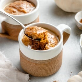 spooning up a vegan pumpkin mug cake from a mug