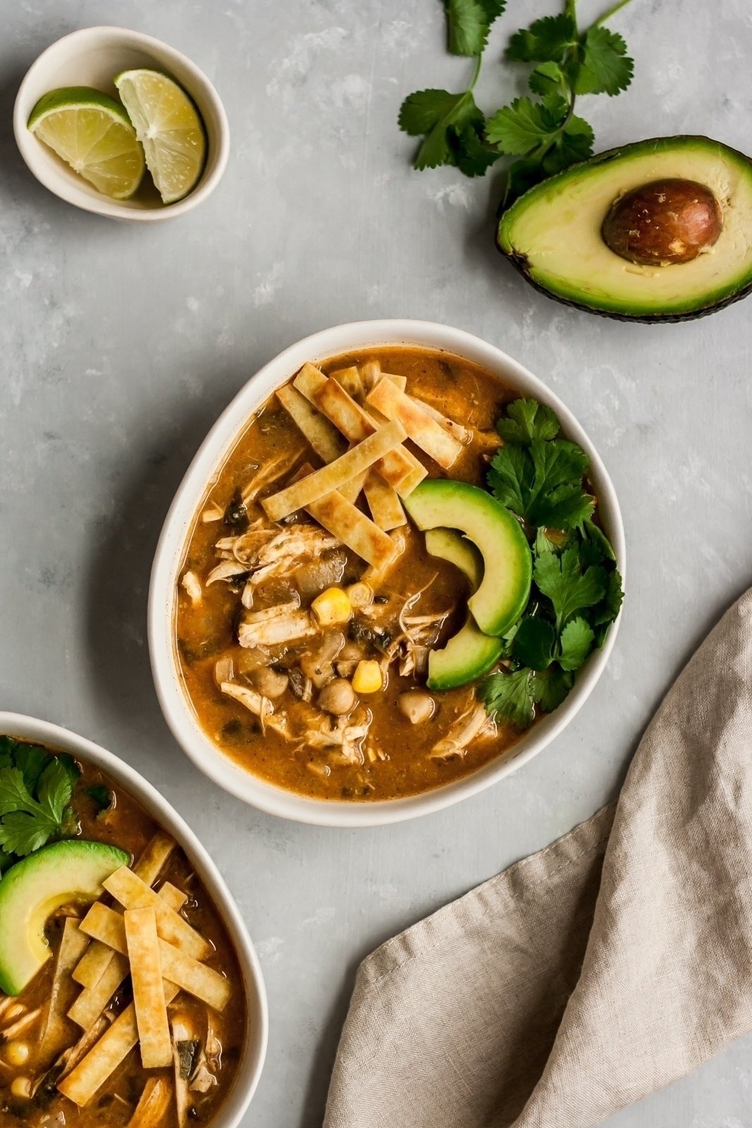 healthy white chicken chili in a white bowl next to a dish of lime wedges and half of an avocado