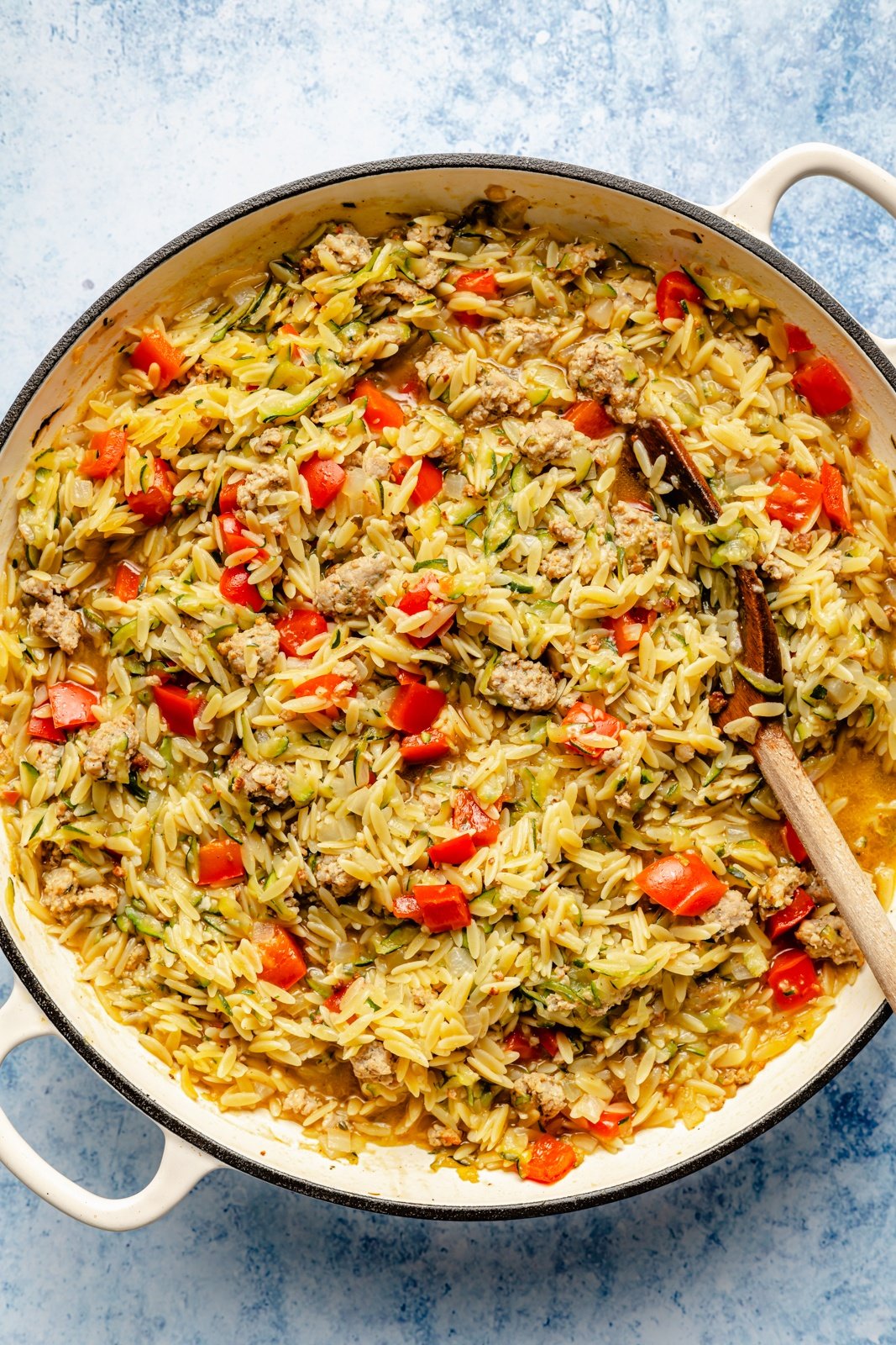 cooking zucchini and sausage baked orzo in a skillet